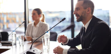 Young successful delegate in formalwear talking to microphone while asking questions of audience